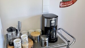 Un carrito de café con diverso equipo y recipientes para prepararlo, incluyendo una cafetera, un molinillo y varias tazas y termos.