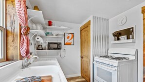 Una cocina con un lavamanos blanco, estufa, microondas y una puerta de madera.