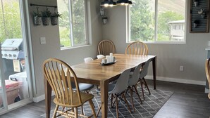 Een eetgedeelte met een houten tafel, stoelen, een vloerkleed en een bordje met daarop keuken.