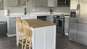 Een moderne keuken met grijze kastjes, een houten eiland met twee stoelen, een roestvrijstalen koelkast en een magnetron.