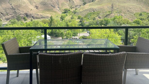 Een glazen tafel met rieten stoelen op een balkon met uitzicht op een bergachtig landschap.