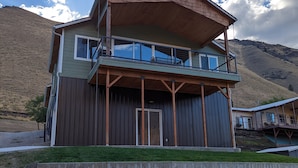 Een twee verdiepingen tellend huis met een balkon, een houten terras en uitzicht op een berg.