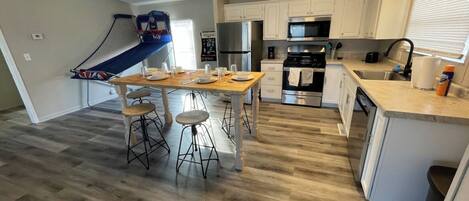 A modern kitchen with white cabinets, stainless steel appliances, and a dining area with stools.