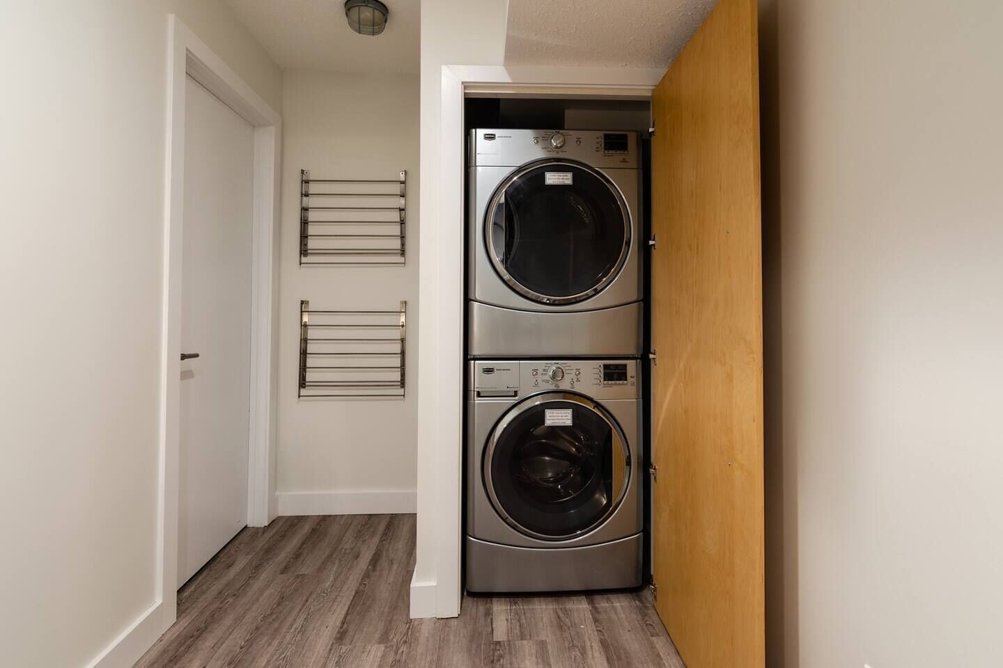 Un lavadero con dos lavadoras apiladas de carga frontal, un tendedero de metal y una puerta de madera.
