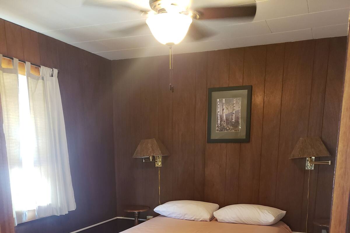 A bedroom with a bed, two bedside lamps, a ceiling fan, and a framed picture on the wall.