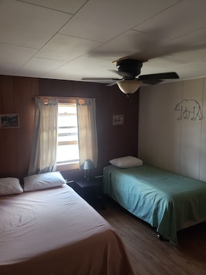 A room with two beds, a ceiling fan, a window with curtains, and a wall with a bear drawing. - lazy bear cabins (South Fork)