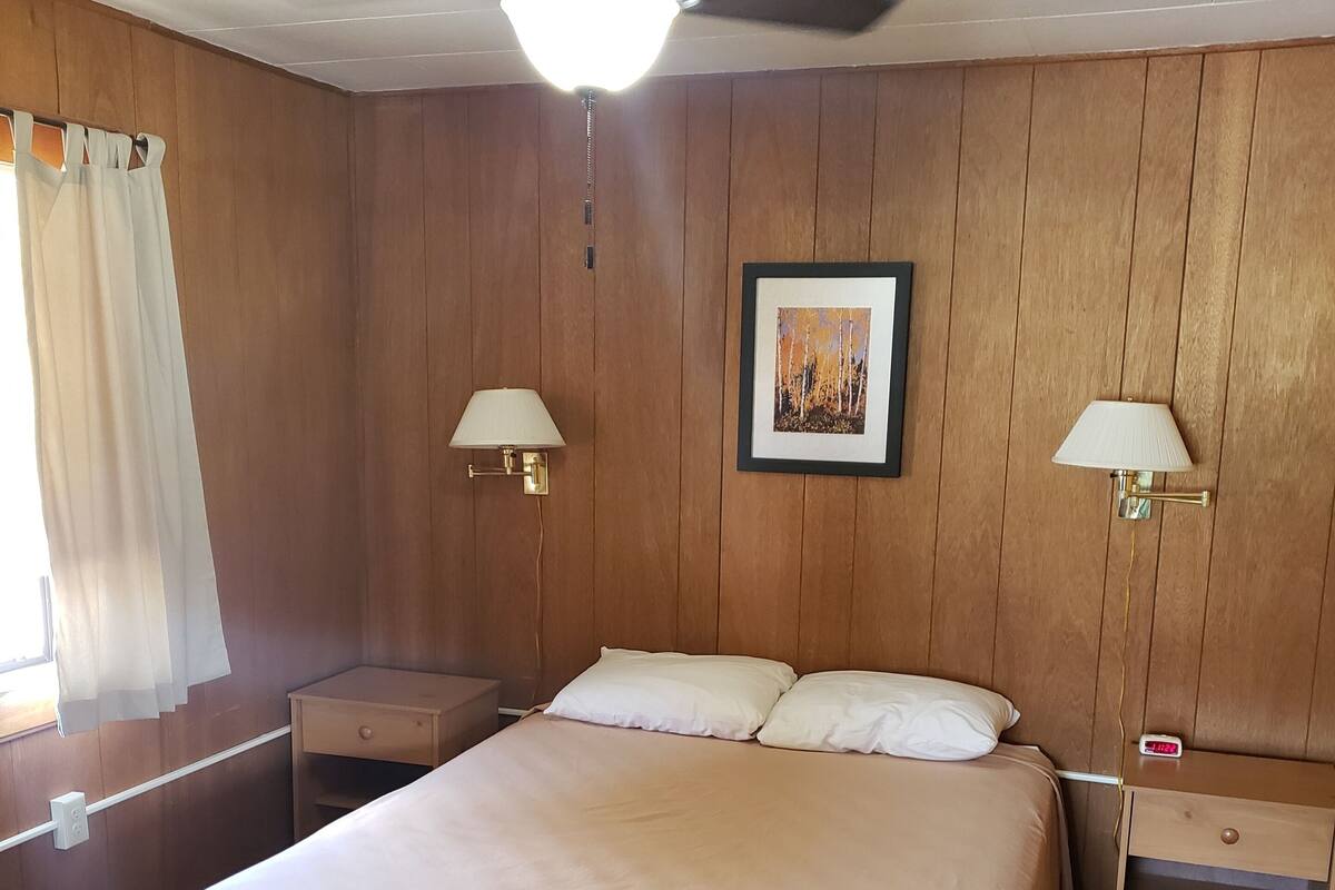 A bedroom with a bed, two bedside tables, a ceiling fan, and two wall-mounted lamps.