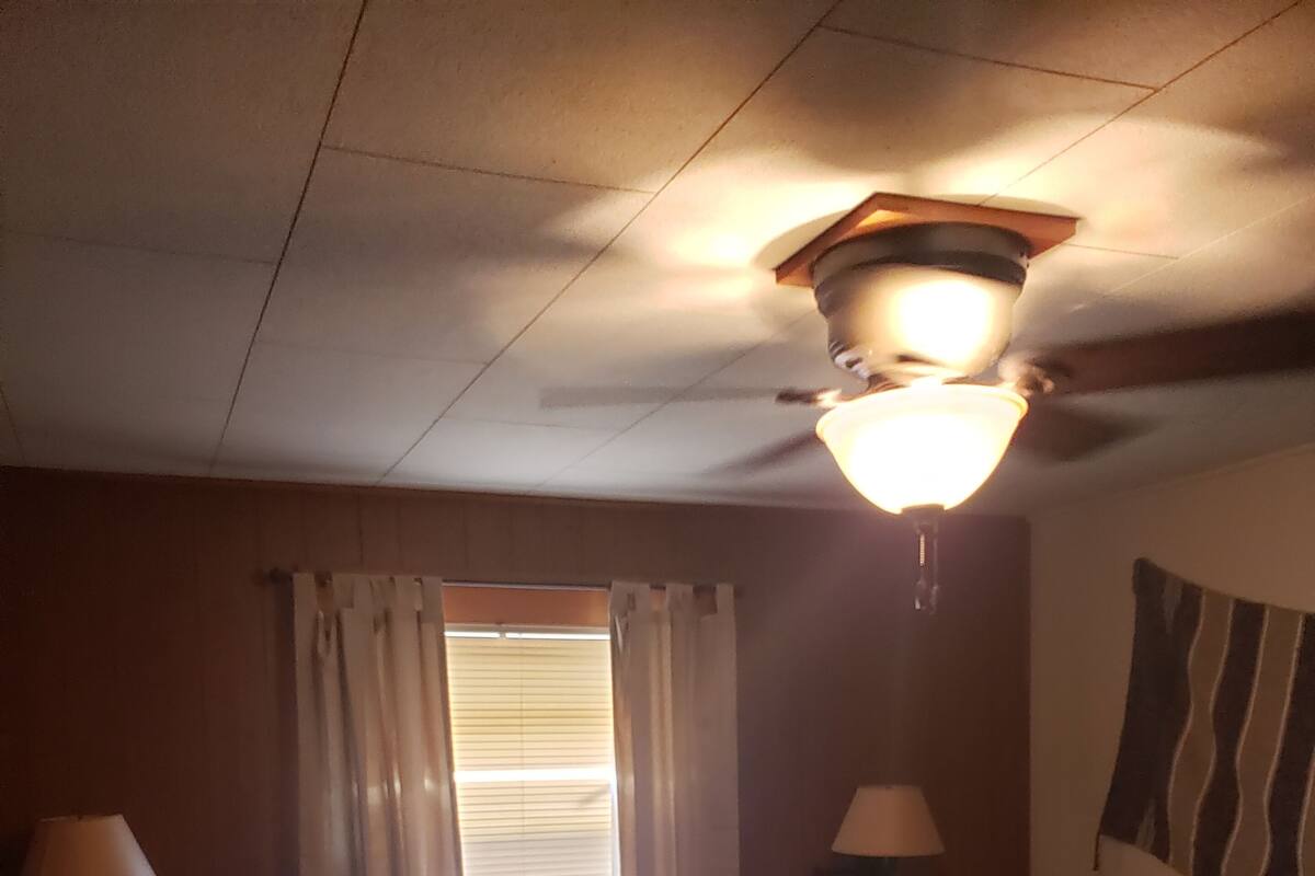A room with two beds, a ceiling fan, a window with curtains, and a wall-mounted lamp.