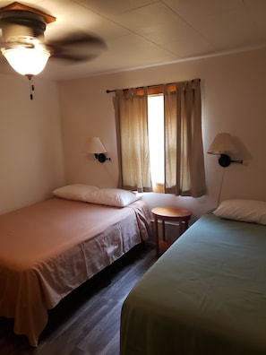 Una habitación con dos camas individuales, una mesita redonda pequeña, un ventilador de techo y dos lámparas de pared.