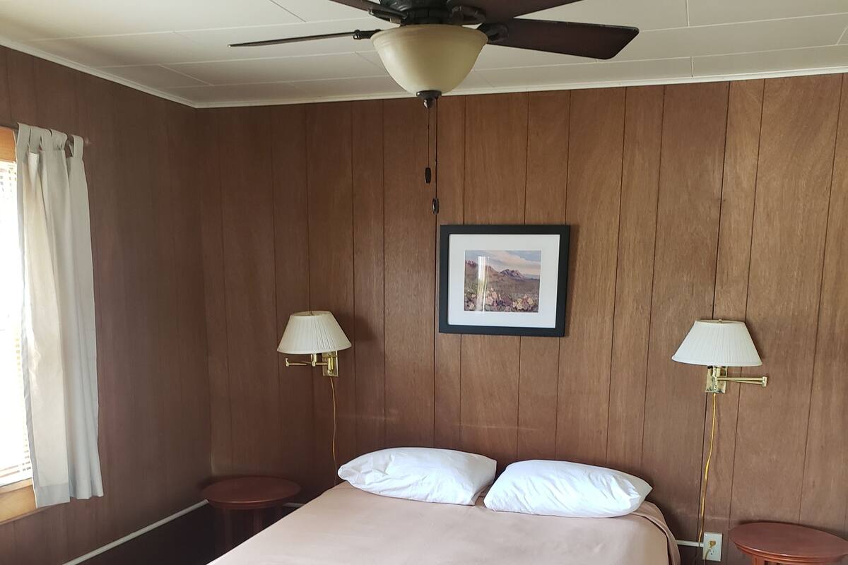 A hotel room with a bed, two bedside tables, a ceiling fan, and a framed picture on the wall.