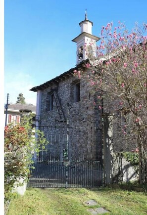 Un edificio de piedra con un campanario, una reja de metal y un árbol en flor.