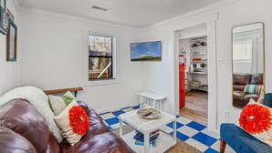Ein Wohnzimmer mit einem braunen Ledersofa, einem weißen Couchtisch, einem blau-weißen karierten Boden, einem Fernseher und einem Spiegel.