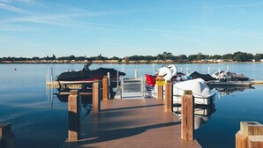 A calm lake with a wooden dock extending into the water. Boats are docked at the pier, and a caution sign is visible.