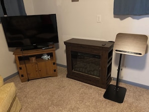 A living room with a flat-screen TV on a wooden stand, a fireplace, and a floor lamp.