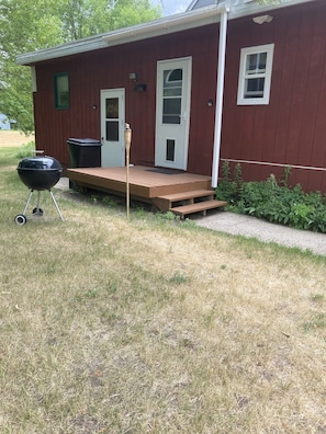 A house with a wooden deck, a barbecue grill, and a trash can.