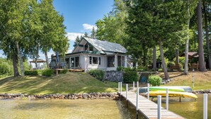 A lakeside cabin with a dock extending into the water, surrounded by trees and a grassy area.