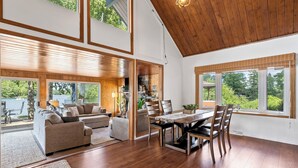 A spacious living area with a dining table and chairs, a sofa, and a view of a lake.