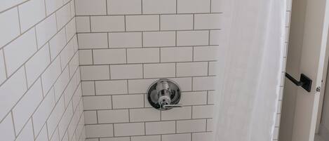 A shower with white tiled walls and a white shower curtain.