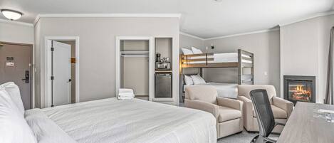 A hotel room with a large bed, a desk with a chair, a sofa, a closet, and a fireplace.