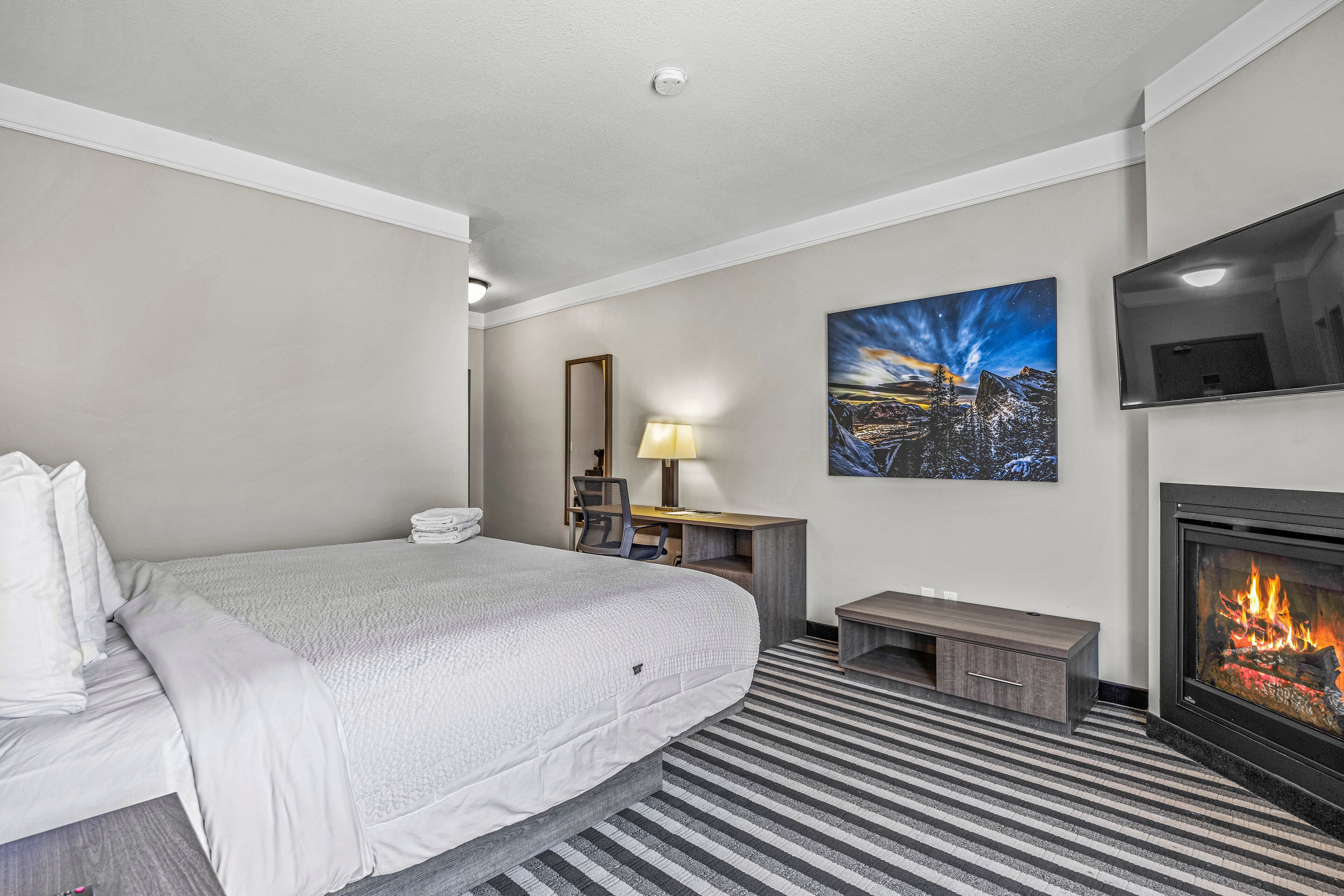 Habitación de hotel con cama, escritorio, silla, lámpara, un cuadro y chimenea.
