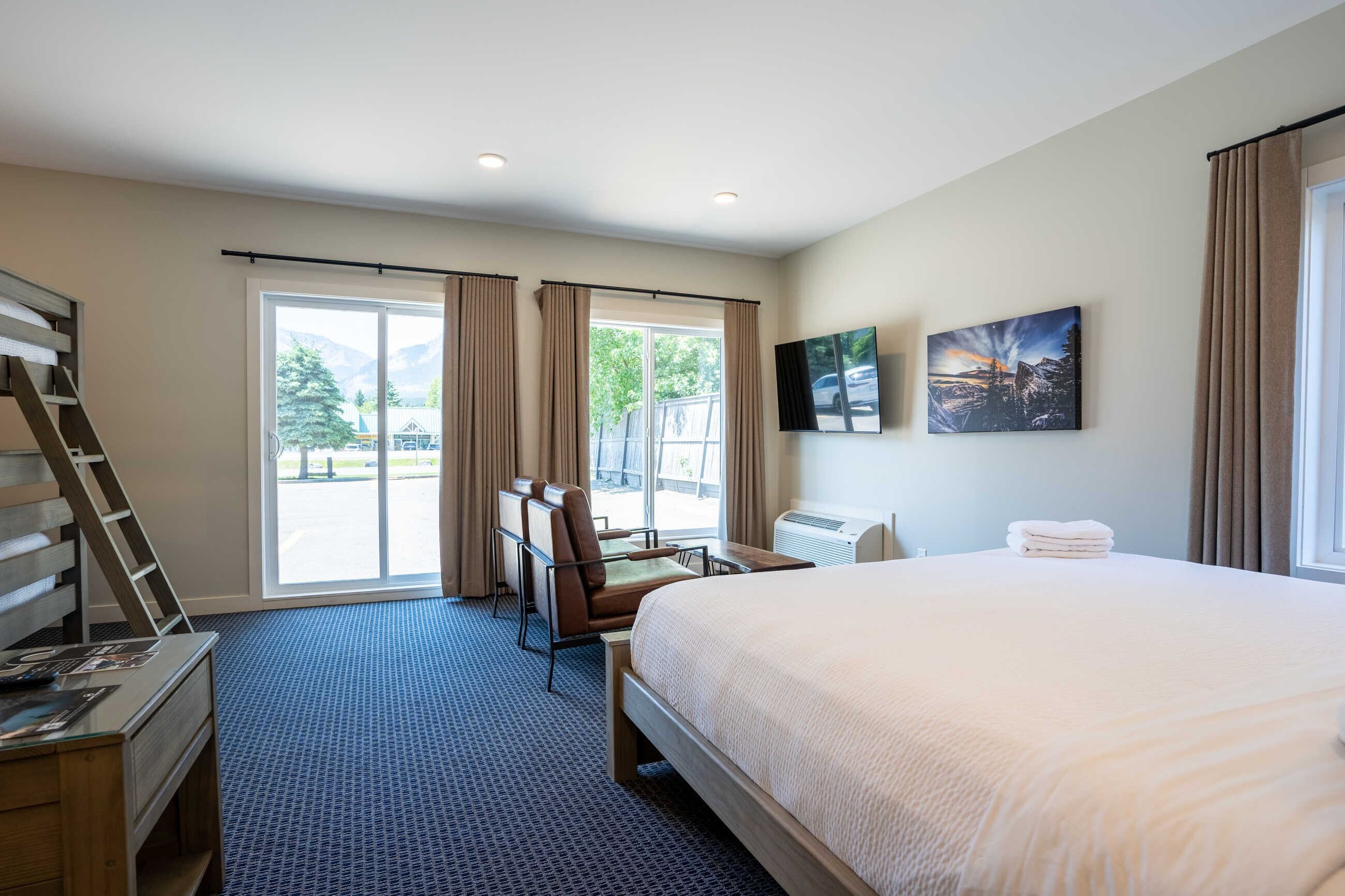 Une chambre d’hôtel avec un grand lit, un bureau, une chaise et une vue sur les montagnes par la fenêtre.