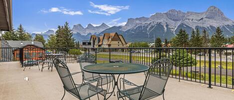 A balcony with outdoor seating, a mountain view, and a building with a sign.