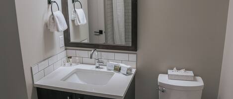 Un bagno moderno con un lavandino bianco, mobili scuri, un water e uno specchio illuminato.