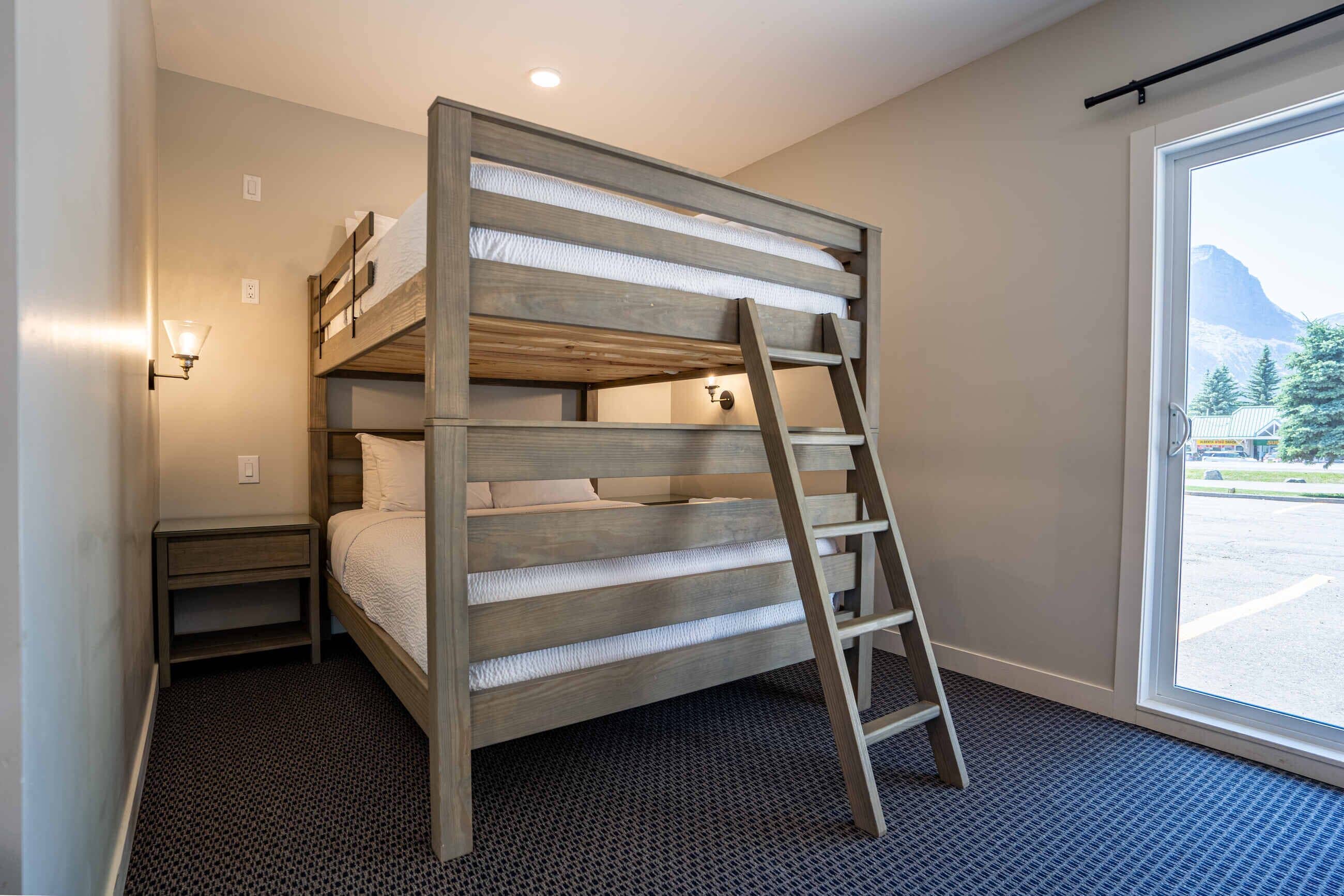 A bunk bed with a ladder, a nightstand, and a window with a mountain view.