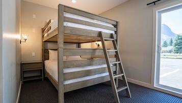 Una cama litera con escalera, una mesita de noche y una ventana con vista a las montañas.