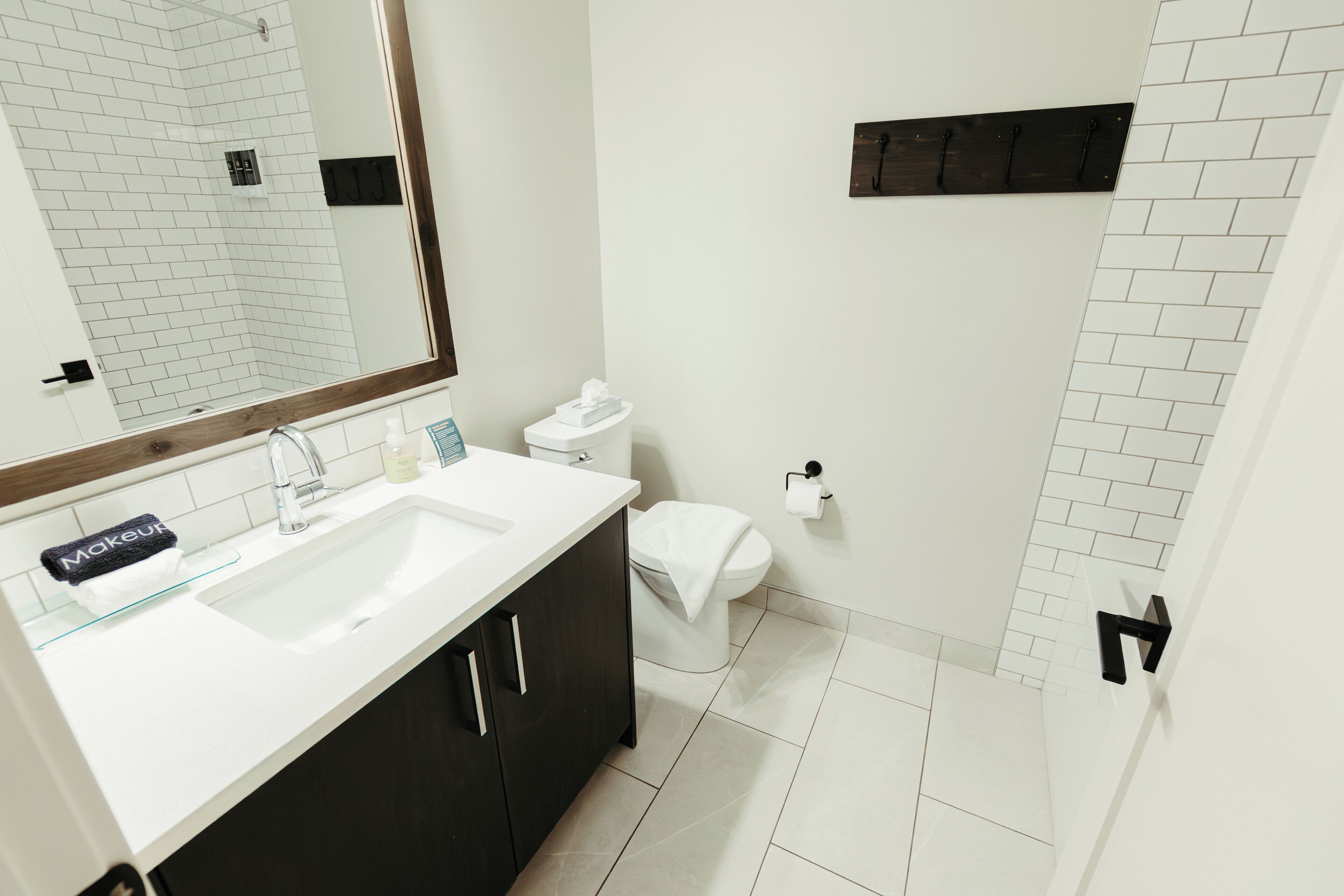 Un baño moderno con un lavamanos blanco, armarios oscuros, un espejo grande y un inodoro blanco.