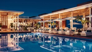 A poolside area with lounge chairs and umbrellas, a bar, and a pool reflecting the surroundings.