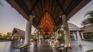 A covered walkway with a thatched roof, palm trees, and a water feature.