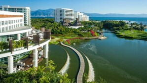 A modern hotel with a riverside view, a bridge, and lush greenery.