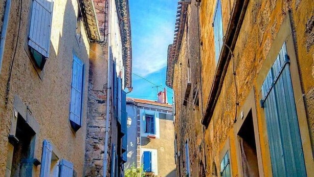 A narrow alleyway with buildings on either side, featuring traditional architecture and shuttered windows.