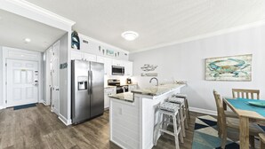 A modern kitchen with white cabinetry, stainless steel appliances, and a central island with bar stools. - Regency Isle 307 | Beachfront | Pools, Hot Tubs and more! | My Beach Getaways (Orange Beach)