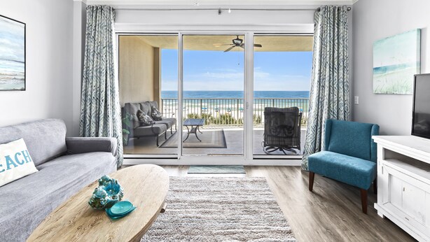 A living room with a view of the beach, a sofa, a coffee table, and a TV stand. - Regency Isle 307 | Beachfront | Pools, Hot Tubs and more! | My Beach Getaways (Orange Beach)