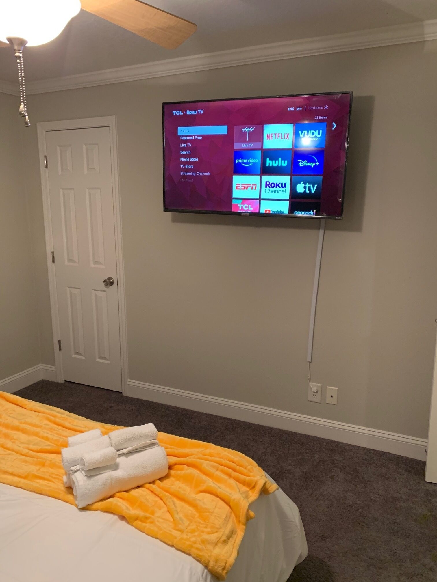 Ein Hotelzimmer mit einem Bett, einem an der Wand befestigten Fernseher, der verschiedene Streaming-Dienste anzeigt, und einer Tür.