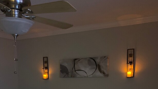 Une chambre d’hôtel comprenant un lit, un ventilateur de plafond, deux appliques murales et une œuvre d’art décorative accrochée au mur.