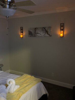 A hotel room with a bed, a ceiling fan, two wall-mounted light fixtures, and a wall art piece. - Good Vibe minutes from downtown Charlotte (Charlotte)
