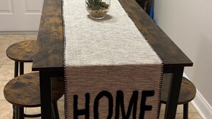 Une table à manger avec un set de table orné du mot « HOME », deux tabourets et une petite plante posée sur la table.