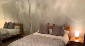 Una habitación de hotel con dos camas, un espejo grande y una mesita de noche con lámpara.