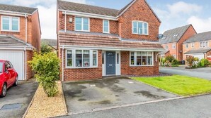 A two-story brick house with a front porch, a garage, and a red car parked in the driveway. - 5 BEDROOM / 4 BATHROOM MODERN DETACHED  wifi  Garden  Parking  Quiet location (Newcastle-under-Lyme)