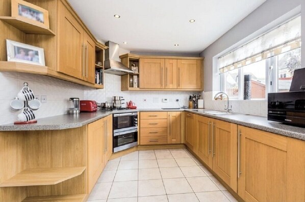 A modern kitchen with wooden cabinets, a built-in oven, and a large window providing natural light. - 5 BEDROOM / 4 BATHROOM MODERN DETACHED wifi Garden Parking Quiet location (Newcastle-under-Lyme)