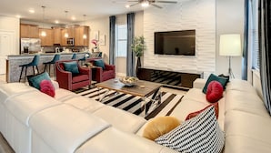 Un salon moderne avec un canapé, des fauteuils, une table basse et un téléviseur fixé au mur.