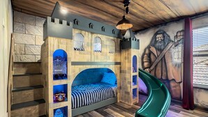 Une chambre à coucher décorée sur le thème d’un château, comprenant un lit, un toboggan et une fresque murale.