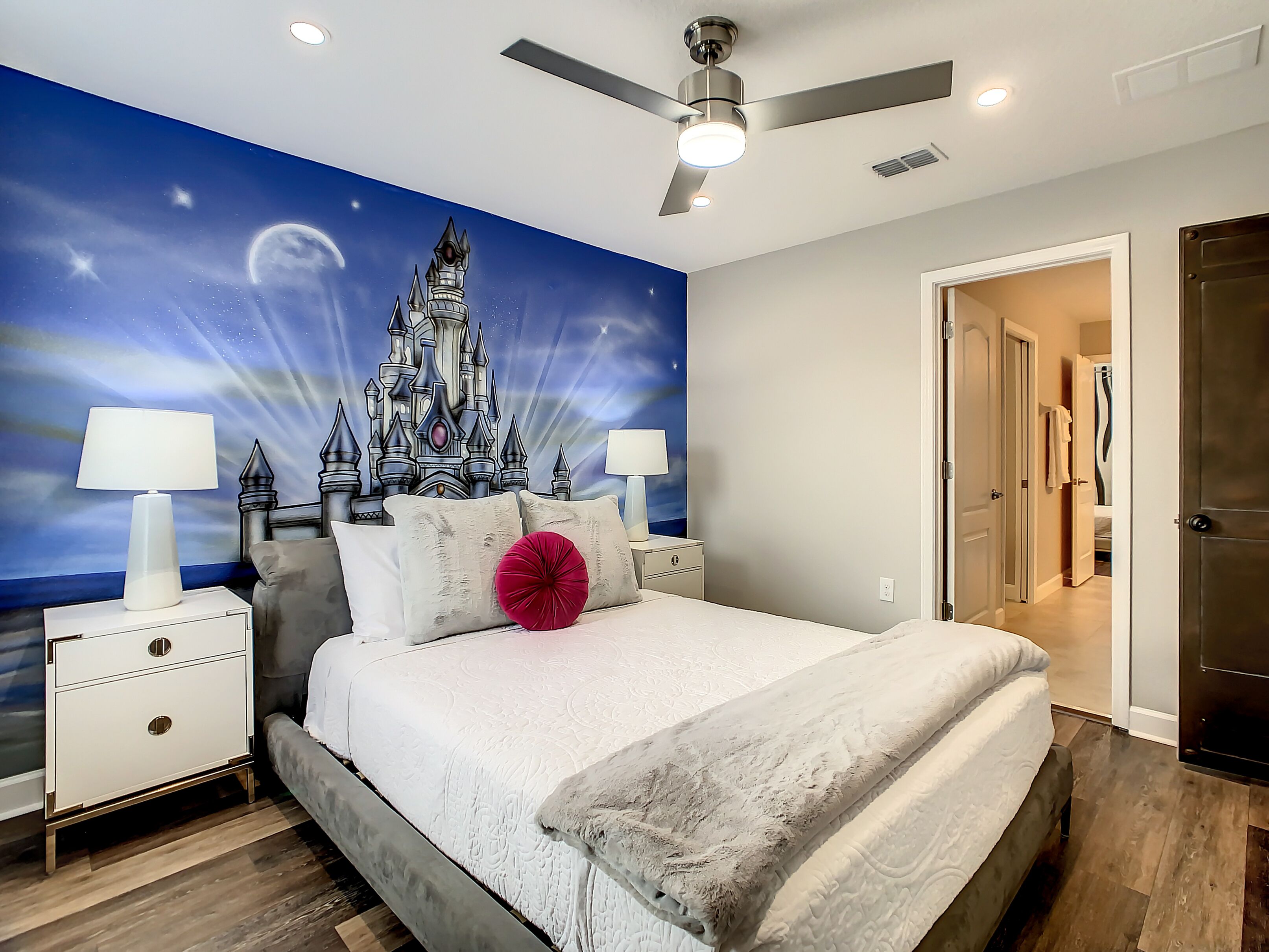 A bedroom with a bed, nightstands, a ceiling fan, and a mural of a castle.