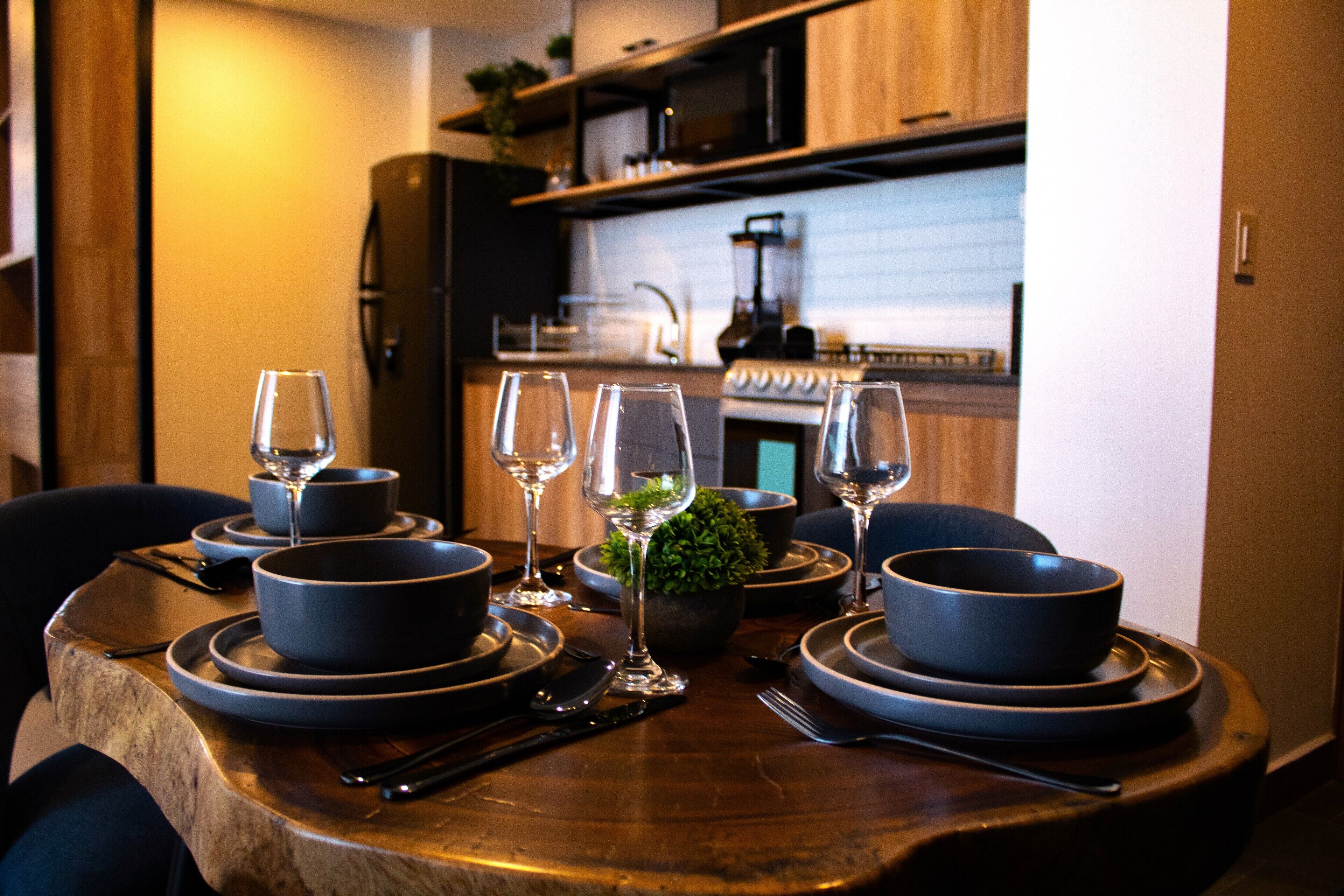 Een eettafel gedekt met blauwe kommen, borden en wijnglazen, met een keuken op de achtergrond.
