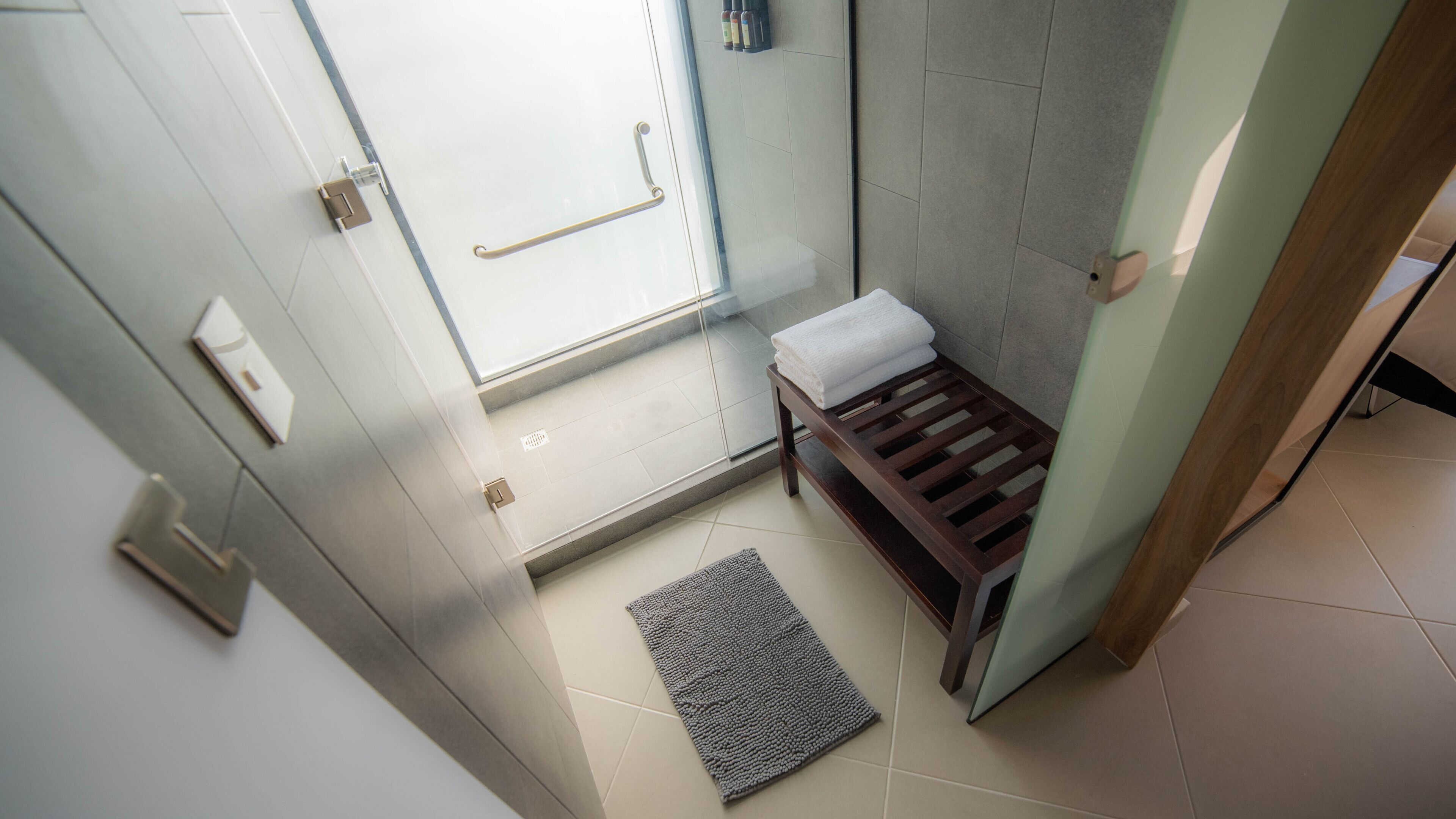 Un baño moderno con mampara de vidrio, banca de madera y toallero.