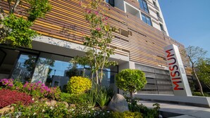 A modern building with a wooden facade, a sign with the name "MISSUN", and a well-maintained garden with various plants and flowers. - Missum Versatile Living (San Andrés Cholula)