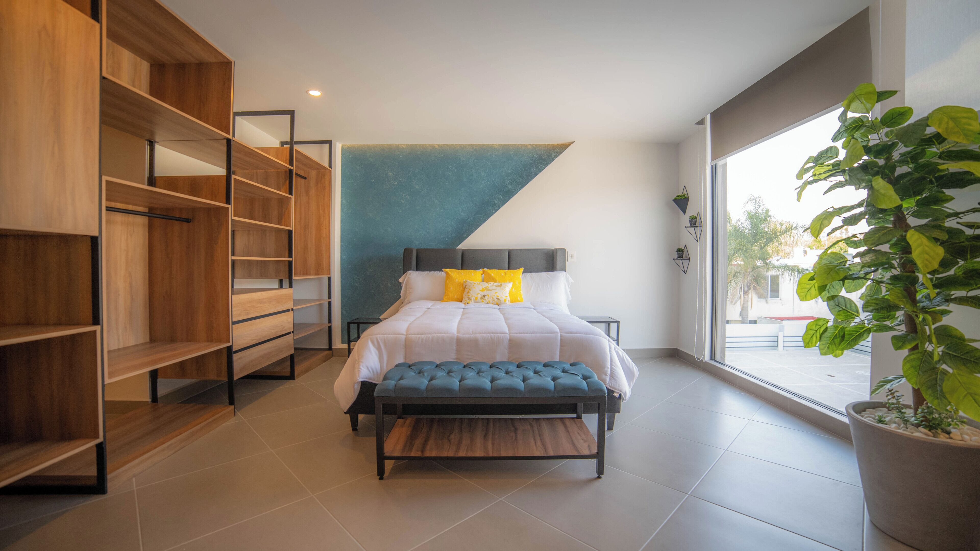 A modern bedroom with a bed, built-in wooden shelving, a large window, and a potted plant.